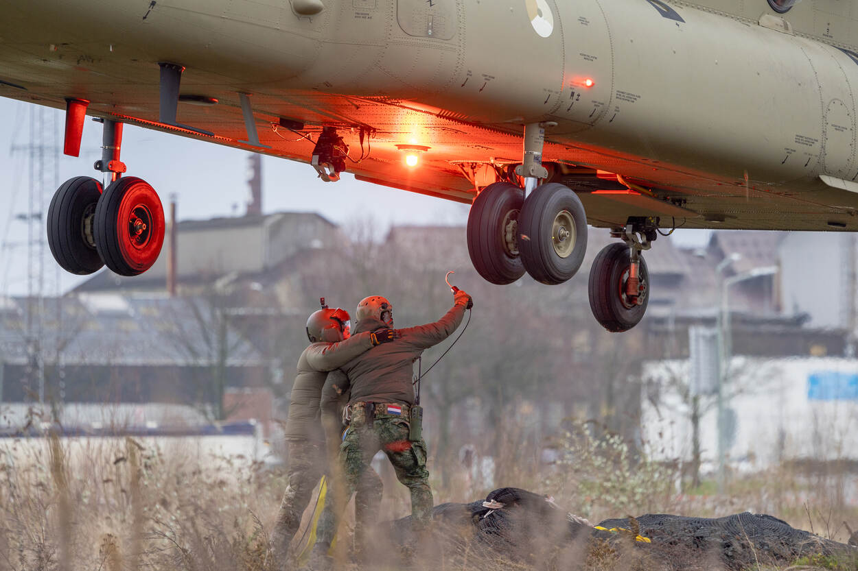 Militairen op de grond bevestigen netten vol stenen aan de Chinook.