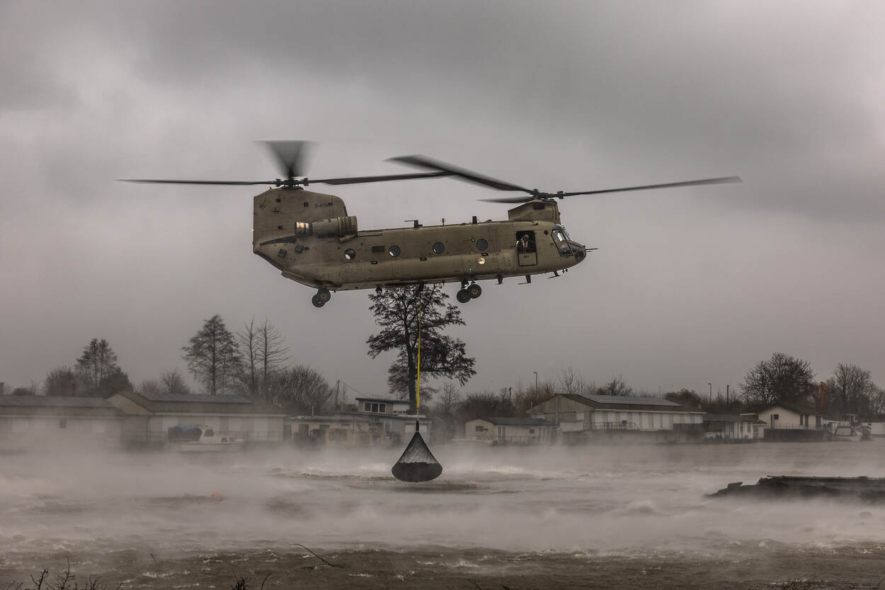 Een Chinook dropt een net vol stenen in het water.