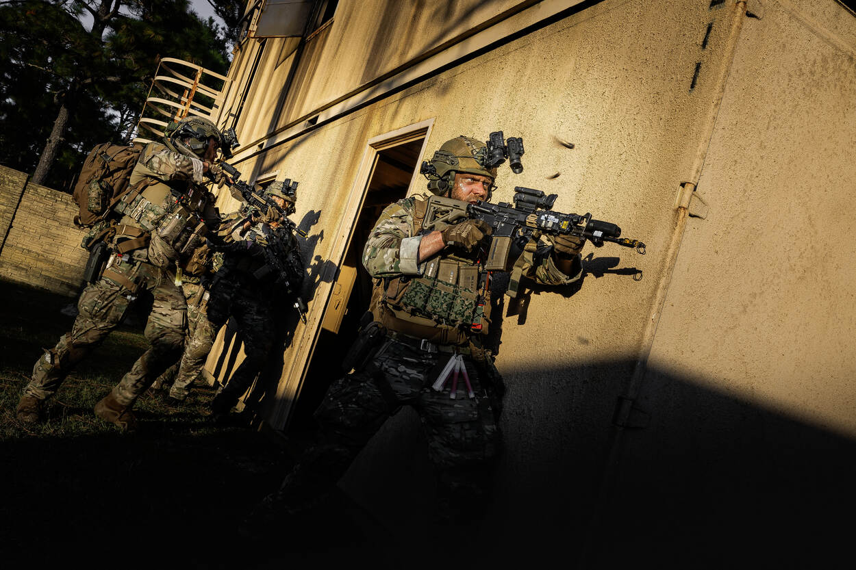 Militairen van de Luchtmobiele brigade bewegen door het oefendorp. Een drietal houdt zich, met getrokken wapen, op voor de ingang van een pand.