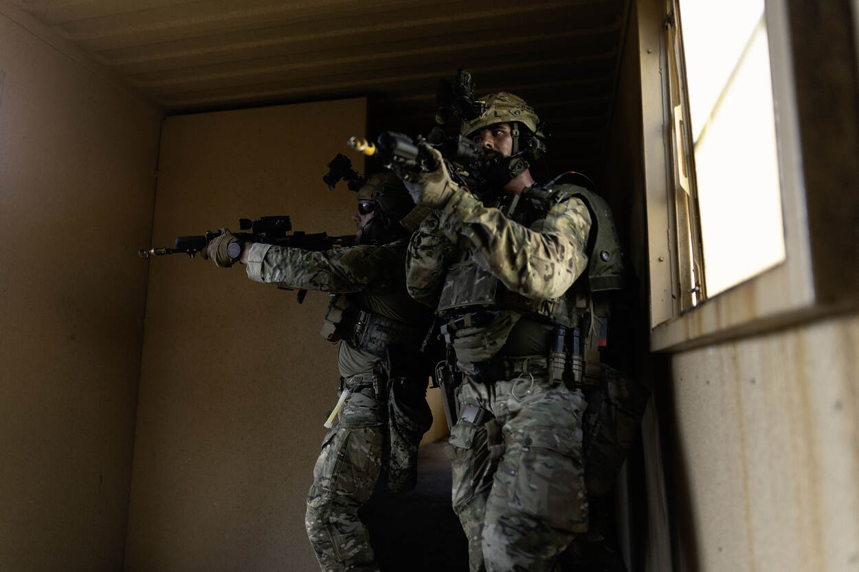 Twee Amerikaanse militairen bewegen door een pand in het Amerikaanse oefendorp, met een lang wapen voor het gezicht.