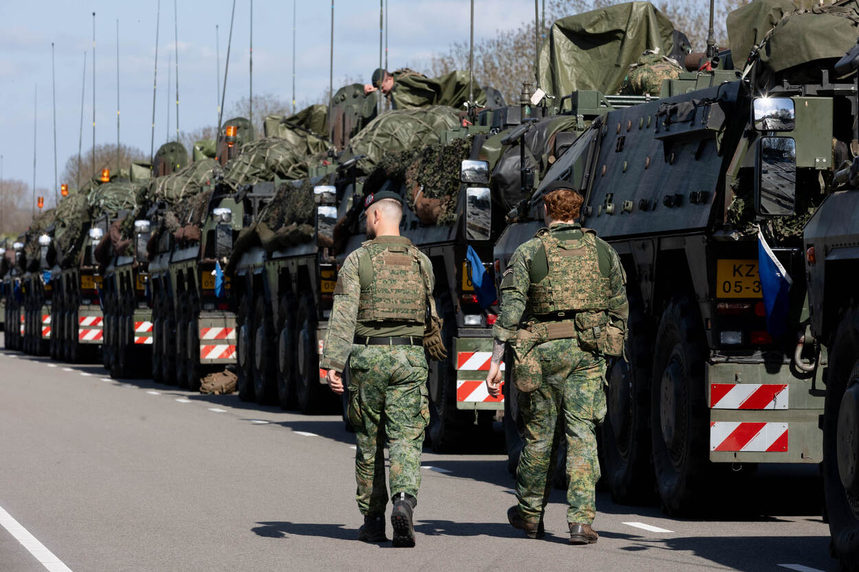 Twee militairen lopen langs een rij militair materieel.