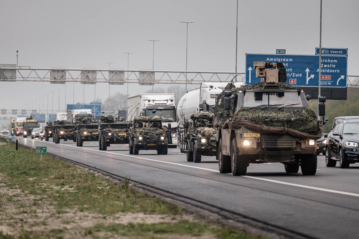 Militaire colonne rijdt op rechterrijstrook over snelweg. Het normale verkeer rijdt op de stroken daarnaast.