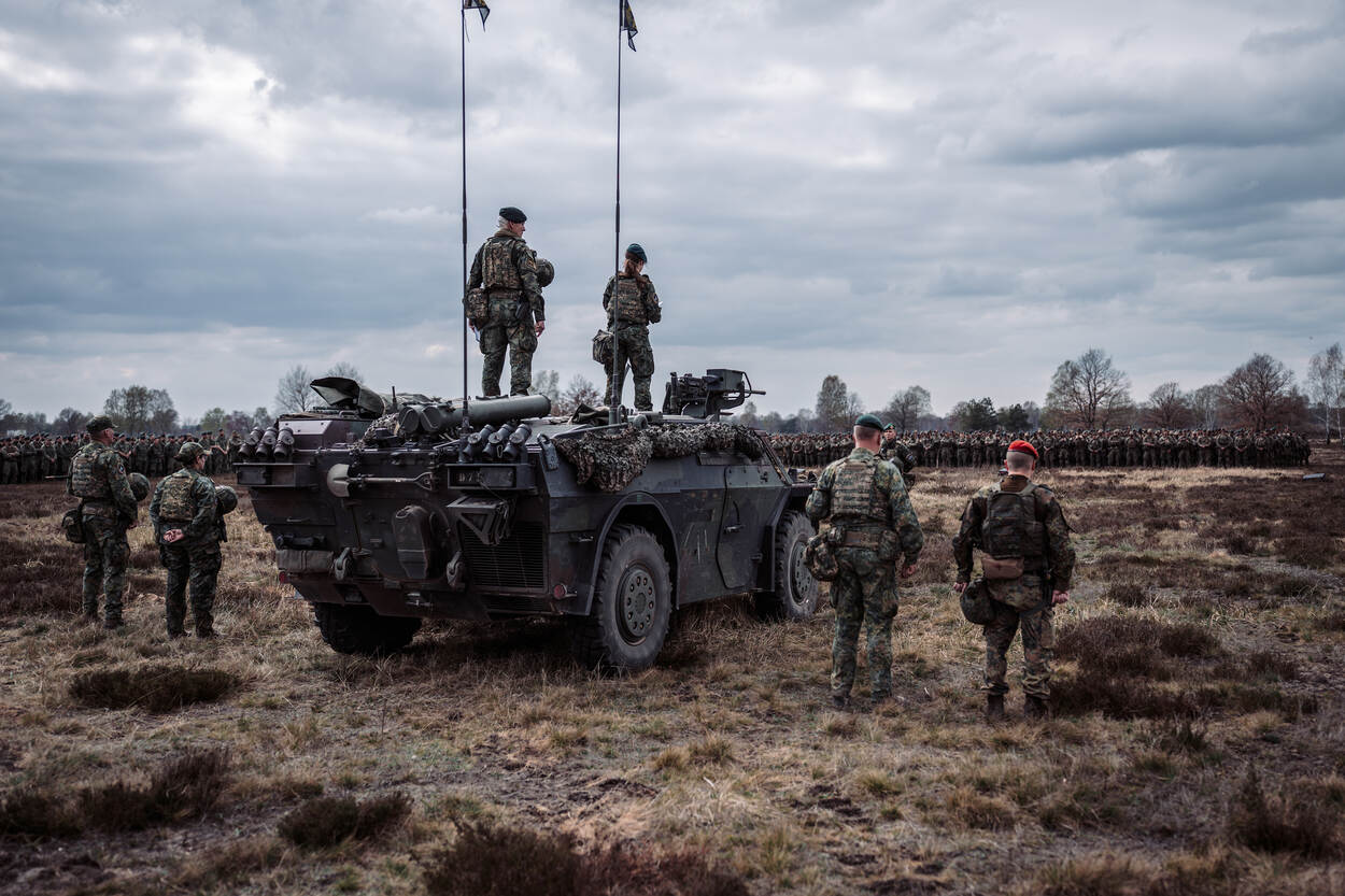 Een enorme groep militairen op de rug gezien, enkelen staan op een voertuig.