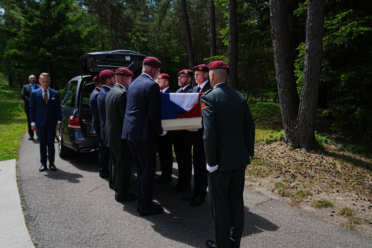 Een kist komt uit de rouwauto, terwijl de draagploeg luchtmobiel in de houding staat voor ontvangst op Veteranenbegraafplaats Loenen.