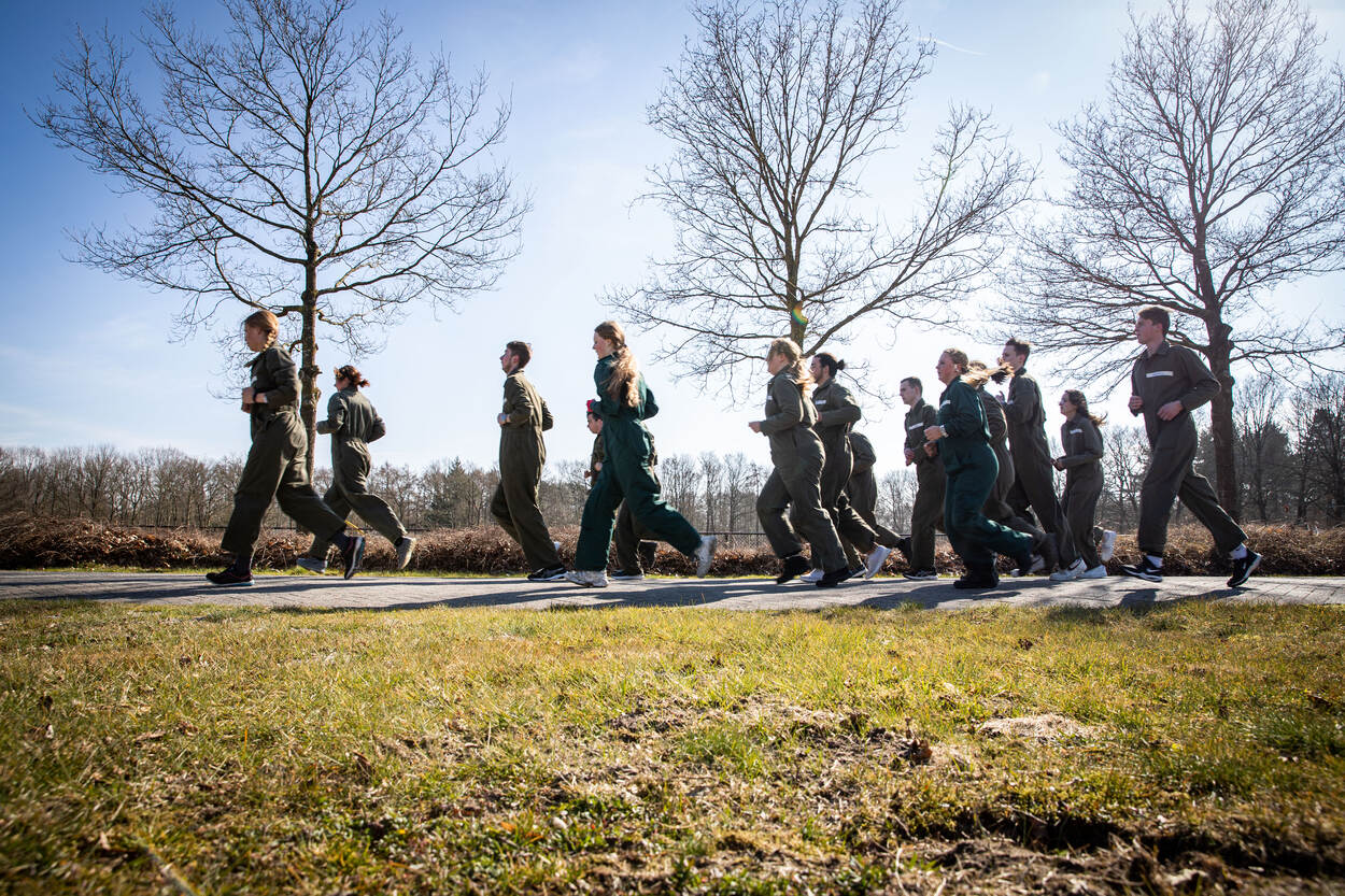 Een groep mensen in groene overall rent voor de camera langs.