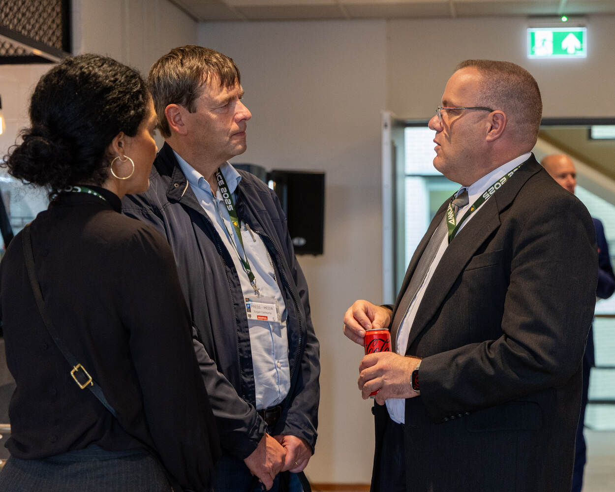 2 mannen en een dame zijn met elkaar in gesprek met op de achtergrond een heer.