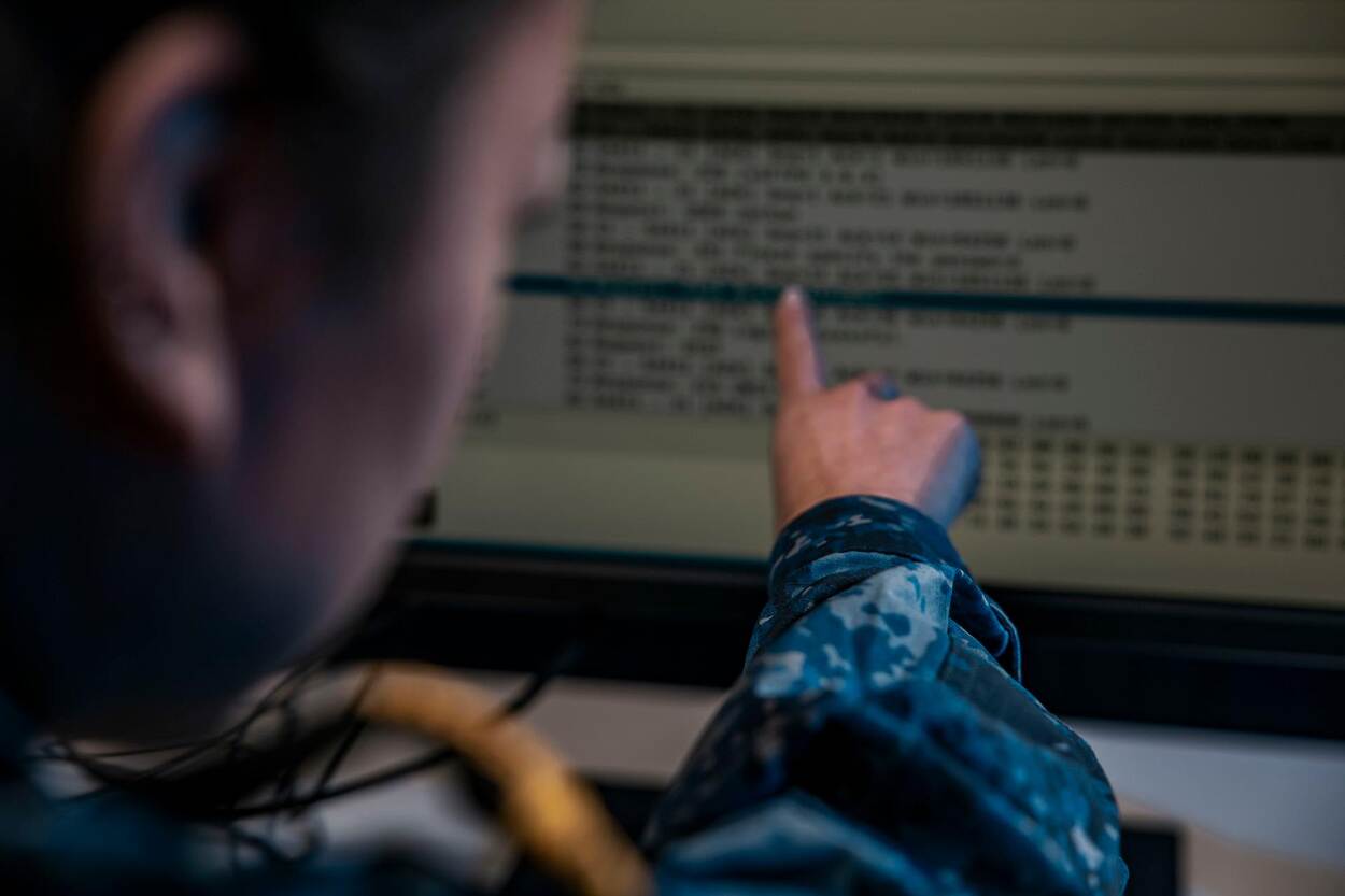 Een militair in marine-uniform wijst naar informatie op een computerscherm.