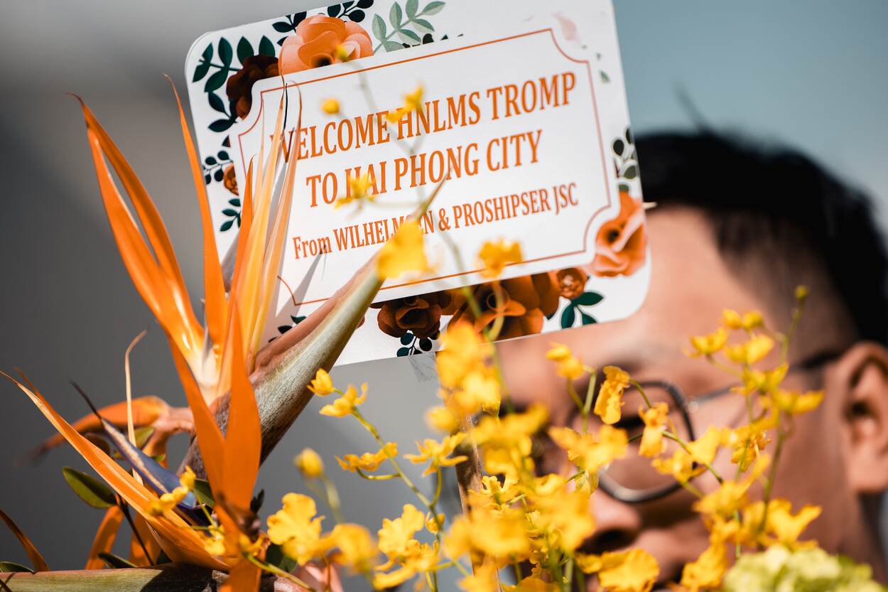 Close up van iemand die een bordje met de tekst ‘Welkom Tromp’ omhoog houdt.