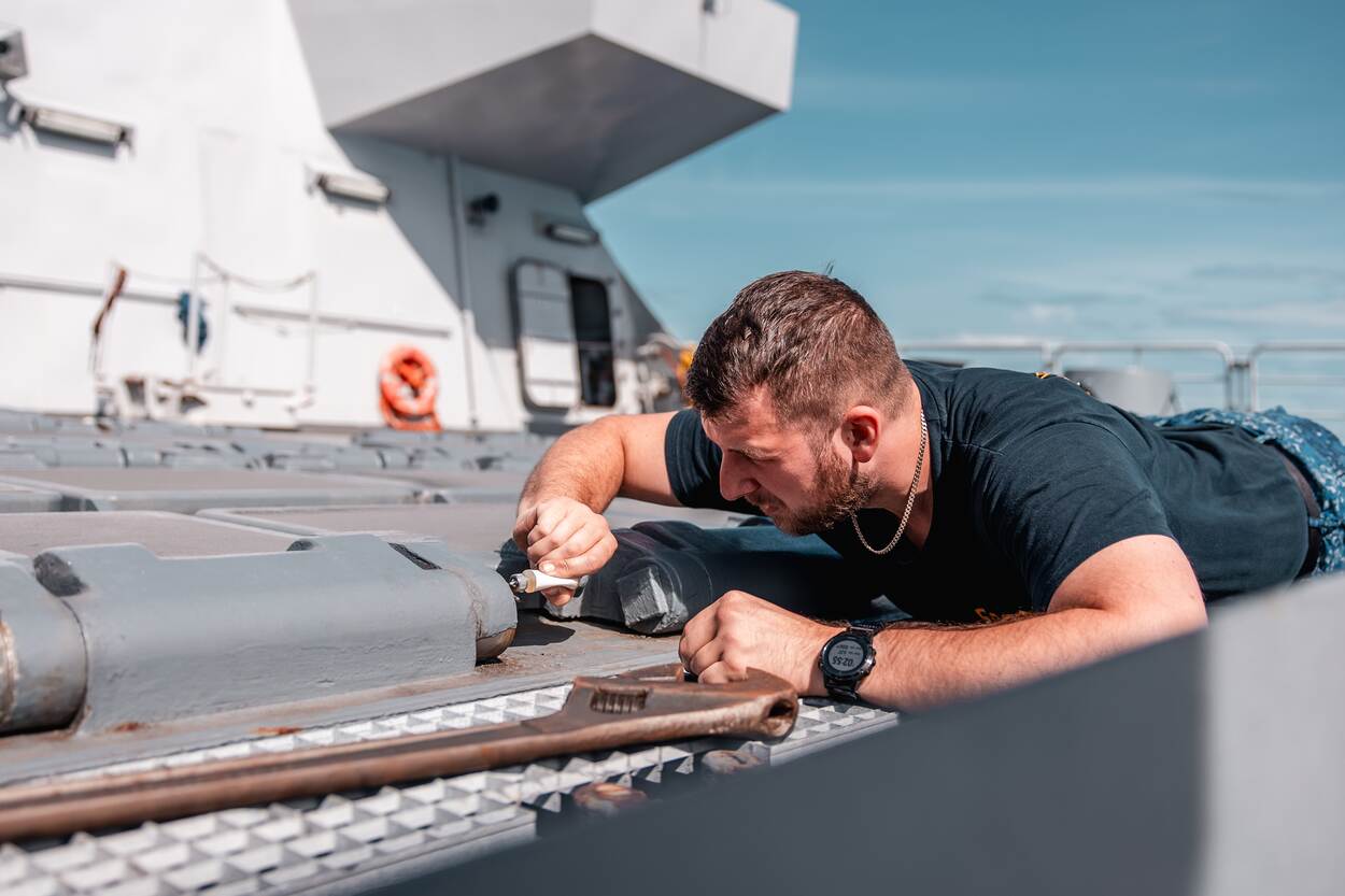 Een techneut vult een smeernippel aan dek.