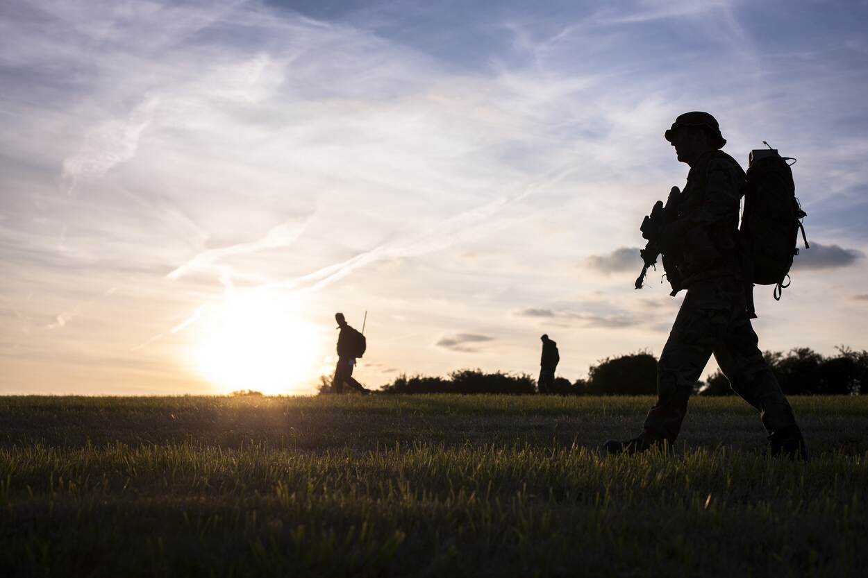 3 mariniers, patrouillerend door een open veld met volle bepakking in de ochtendgloren.