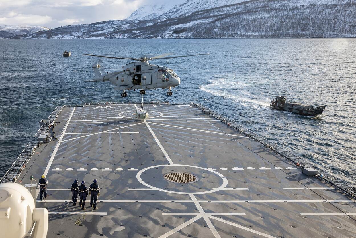 Een NH90 hangt boven het helikopterdek van de Johan de Witt en zet voorraden af.