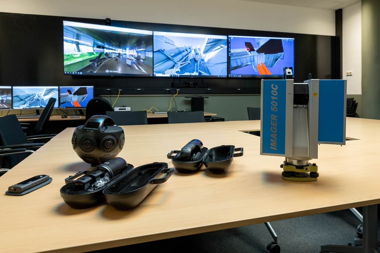 3 openstaande schermen met scanapparatuur op een bureautafel.