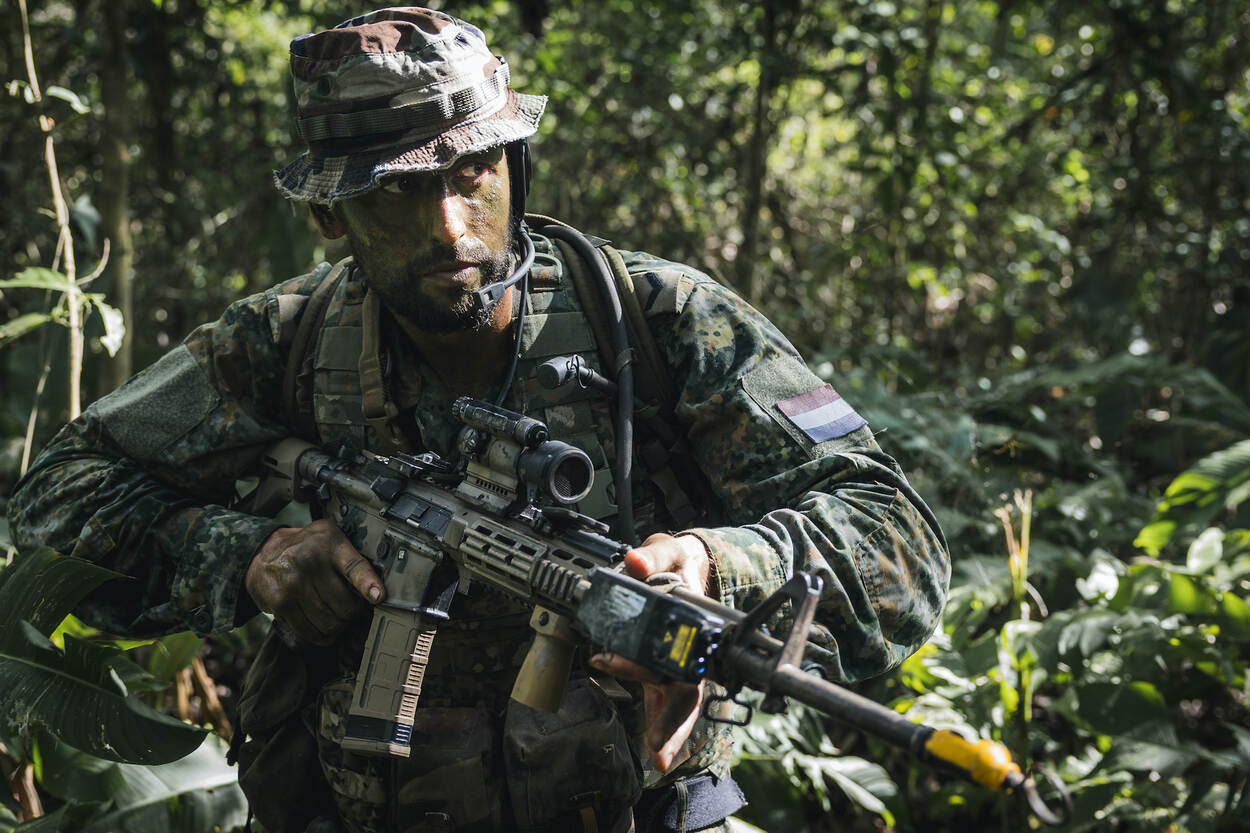 Een Nederlandse marinier baant zich met zijn geweer in de aanslag een weg door de bush.