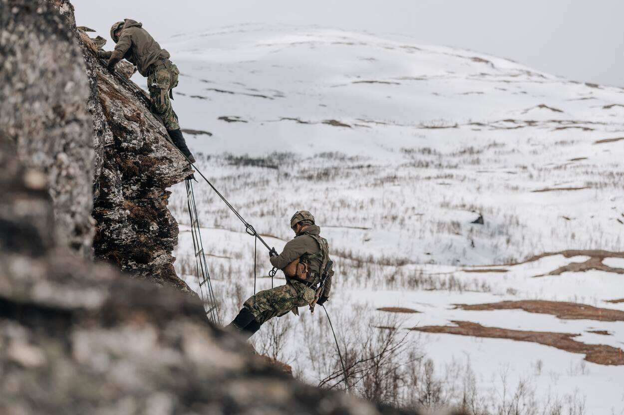 Mariniers dalen van een berg af in een besneeuwd landschap.