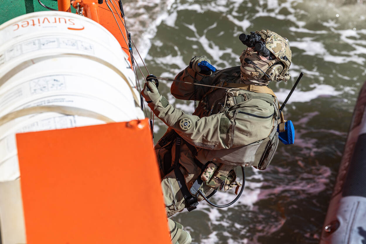 Een operator klimt met een getrokken pistool aan boord van een schip.