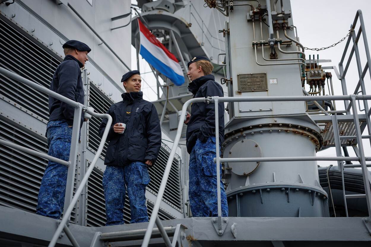 3 jongens in marine-uniform drinken buiten op het schip een kop koffie.