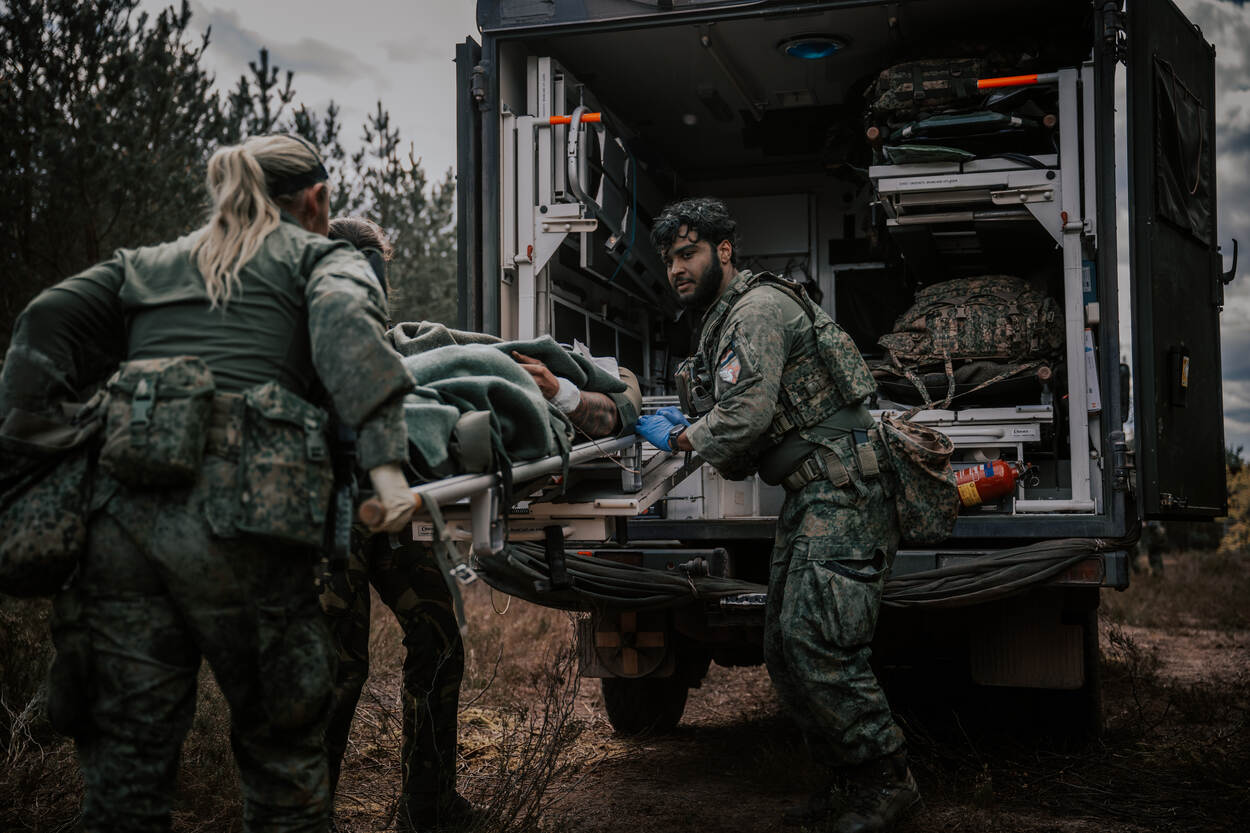 Militairen tillen een gewonde collega op een brancard de achterzijde van de ziekenauto in in het bos.