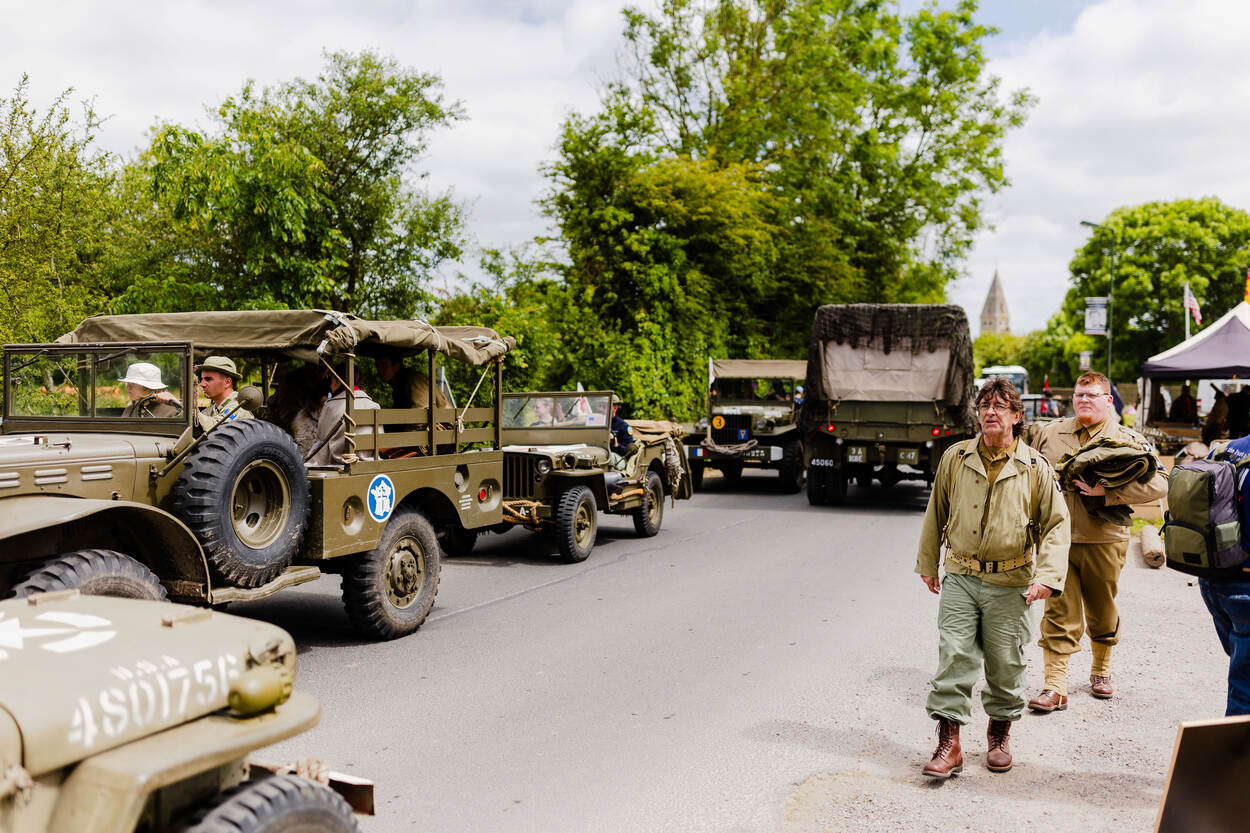 Jeeps uit de Tweede Wereldoorlog rijden door een smalle straat. In de berm lopen personen die verkleed zijn in uniformen uit die tijd.