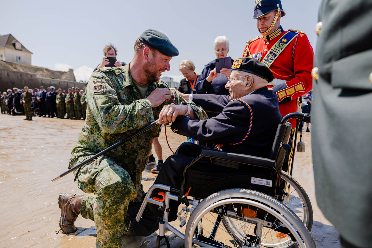 Een fuselier zit geknield voor de rolstoel van veteraan Wolff en neemt zijn koord in ontvangst.