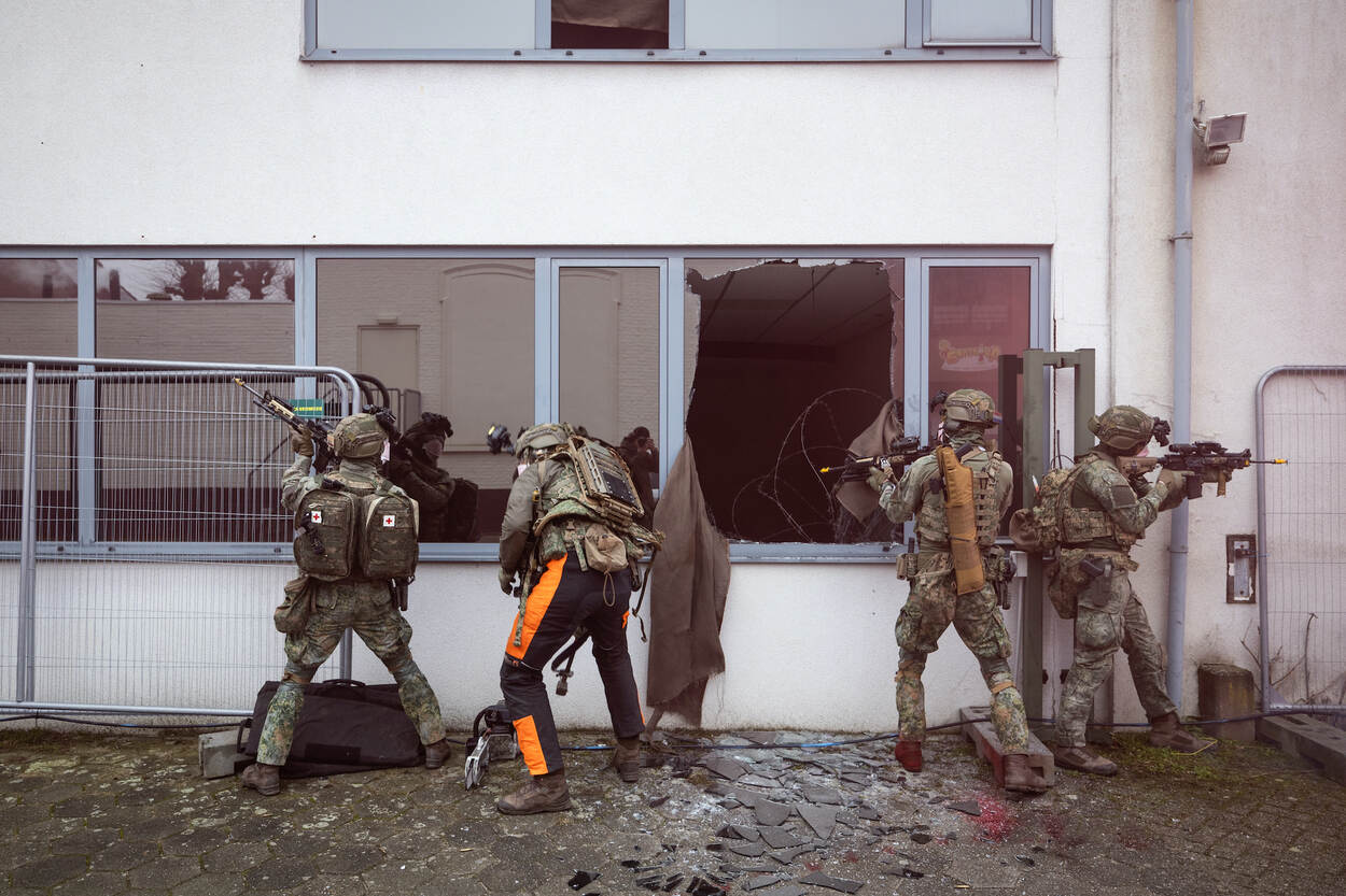 Een groep militairen staat bij een raam, dat net is opengezaagd zodat collega’s naar binnen kunnen.