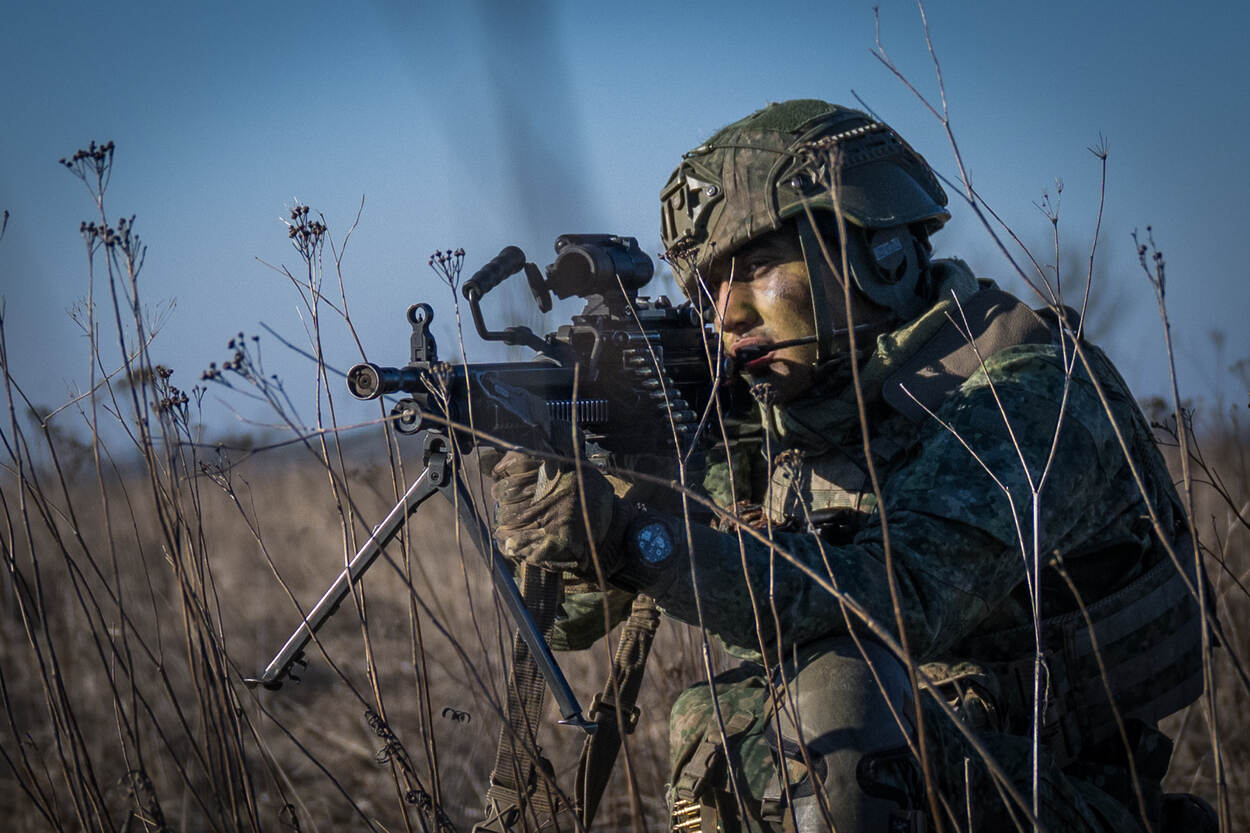 Een geknielde soldaat kijkt door het vizier van zijn minimi.