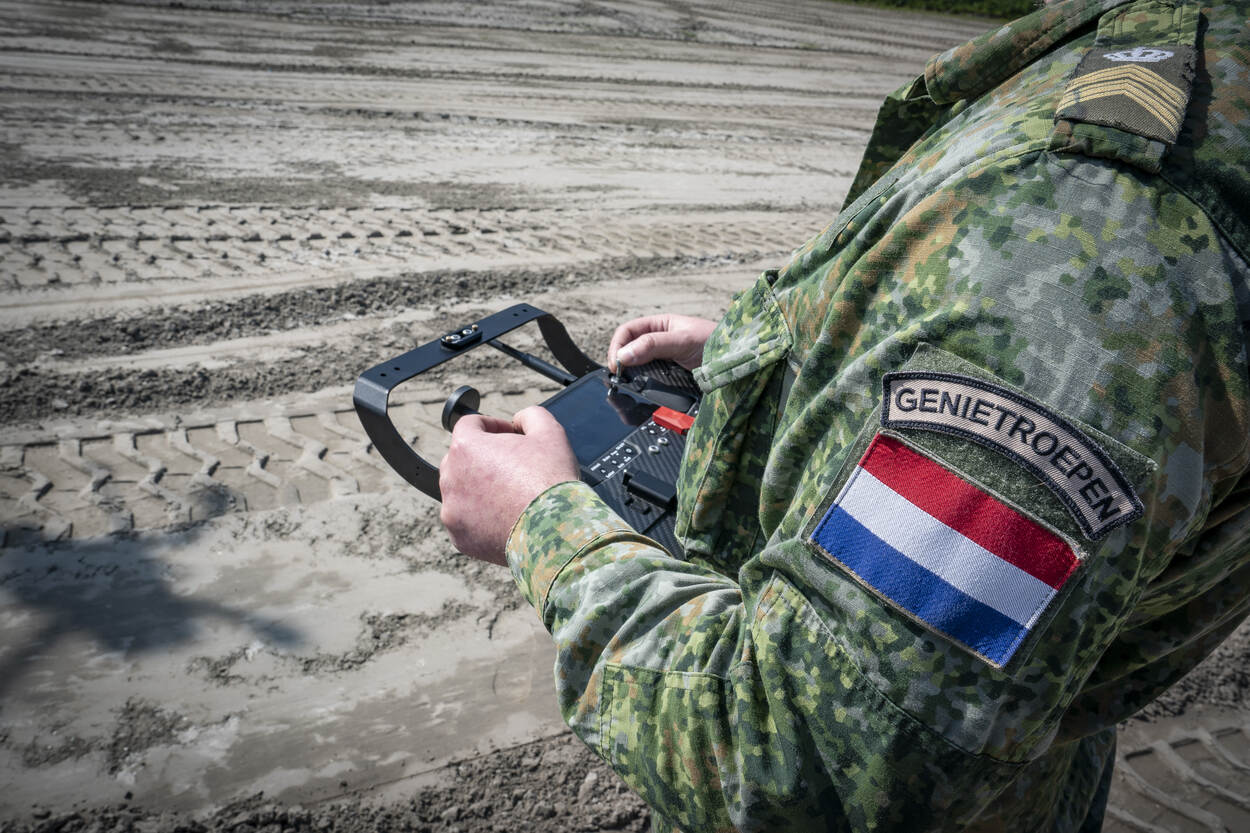 Een militair staat in het zand met een droneconsole in de hand. Het gezicht is niet te zien. Wel prijkt de tekst ‘genietroepen’ op de schouder.