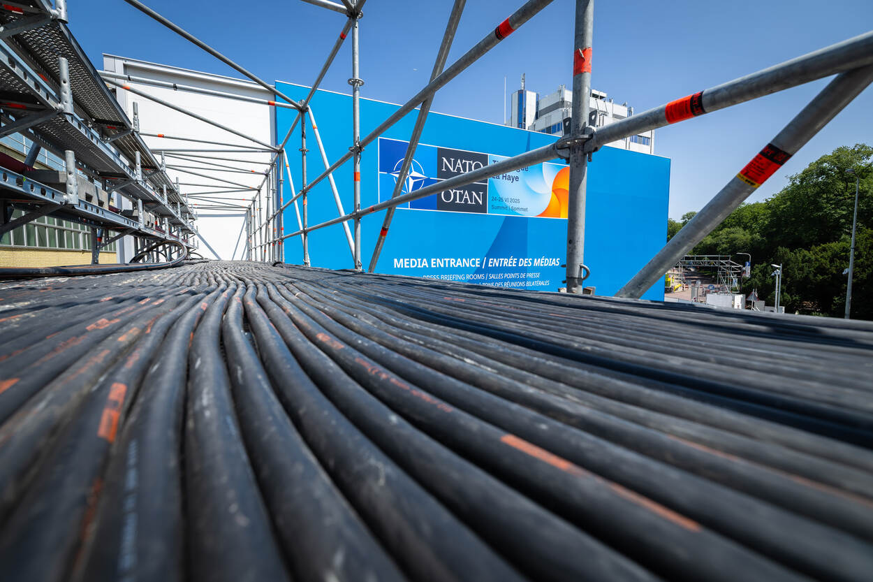 Lange, liggende kabels op een stellage met op achtergrond NAVO-bord.