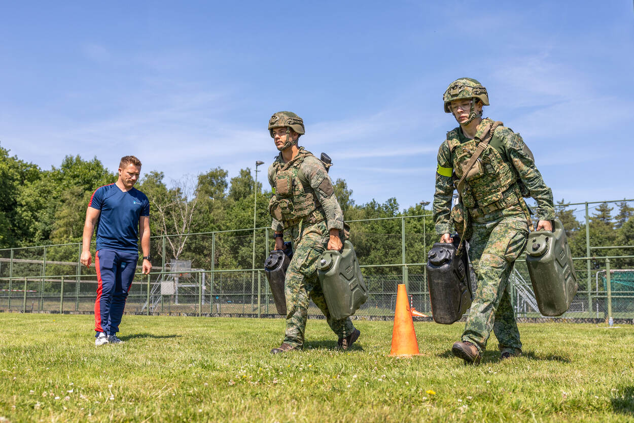 2 militairen dragen volle jerrycans over het veld.