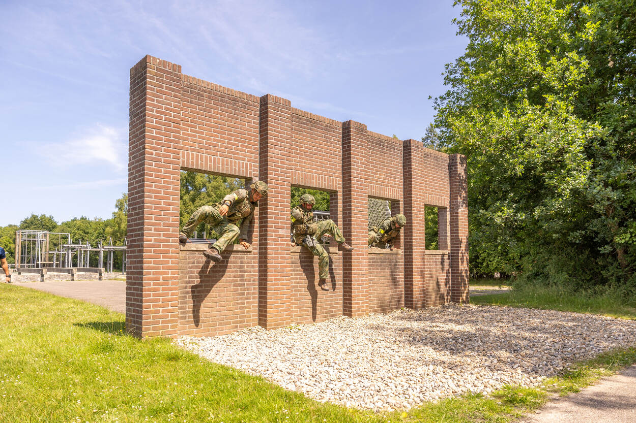 Drie militairen klimmen door een gat in de muur
