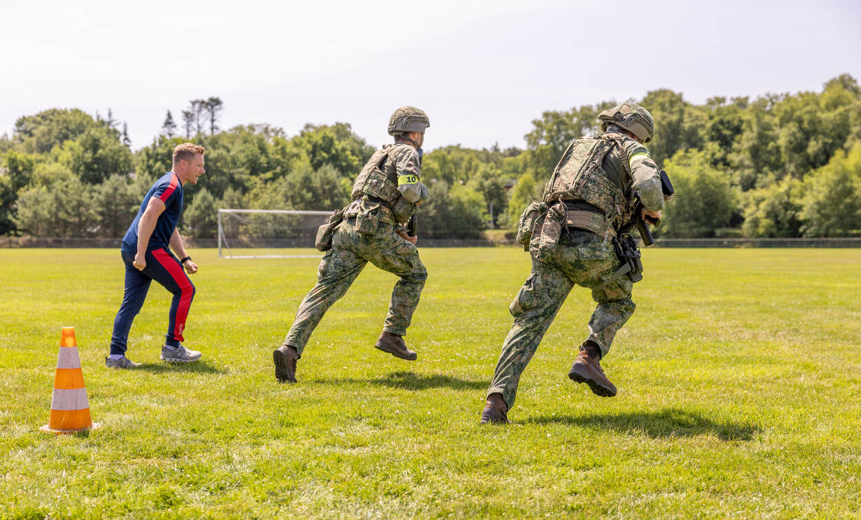 Twee militairen rennen weg, aangemoedigd door hun sportcoach.