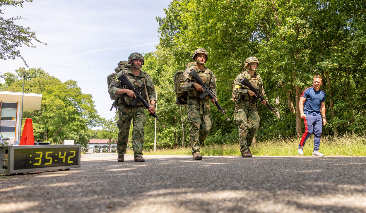 Militairen komen binnen na hun mars onder toeziend oog van hun sportinstructeur.