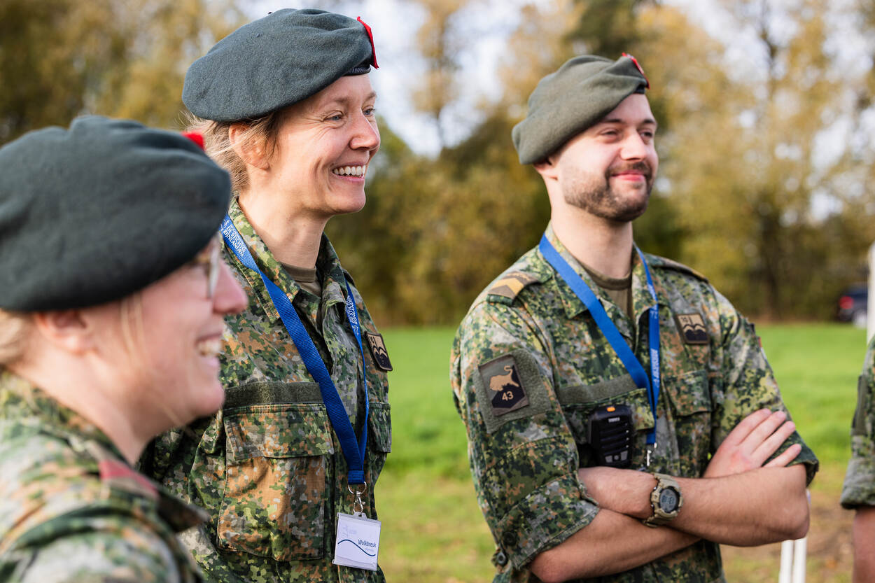3 militairen kijken lachend naar een oefening.