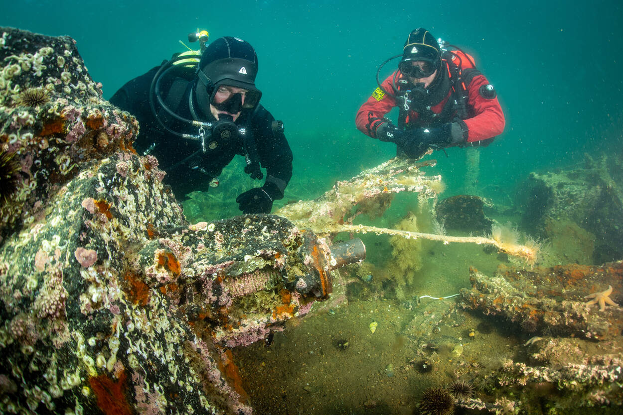 Twee mannen in duikerpak onder water bij de restanten van de Tirpitz.