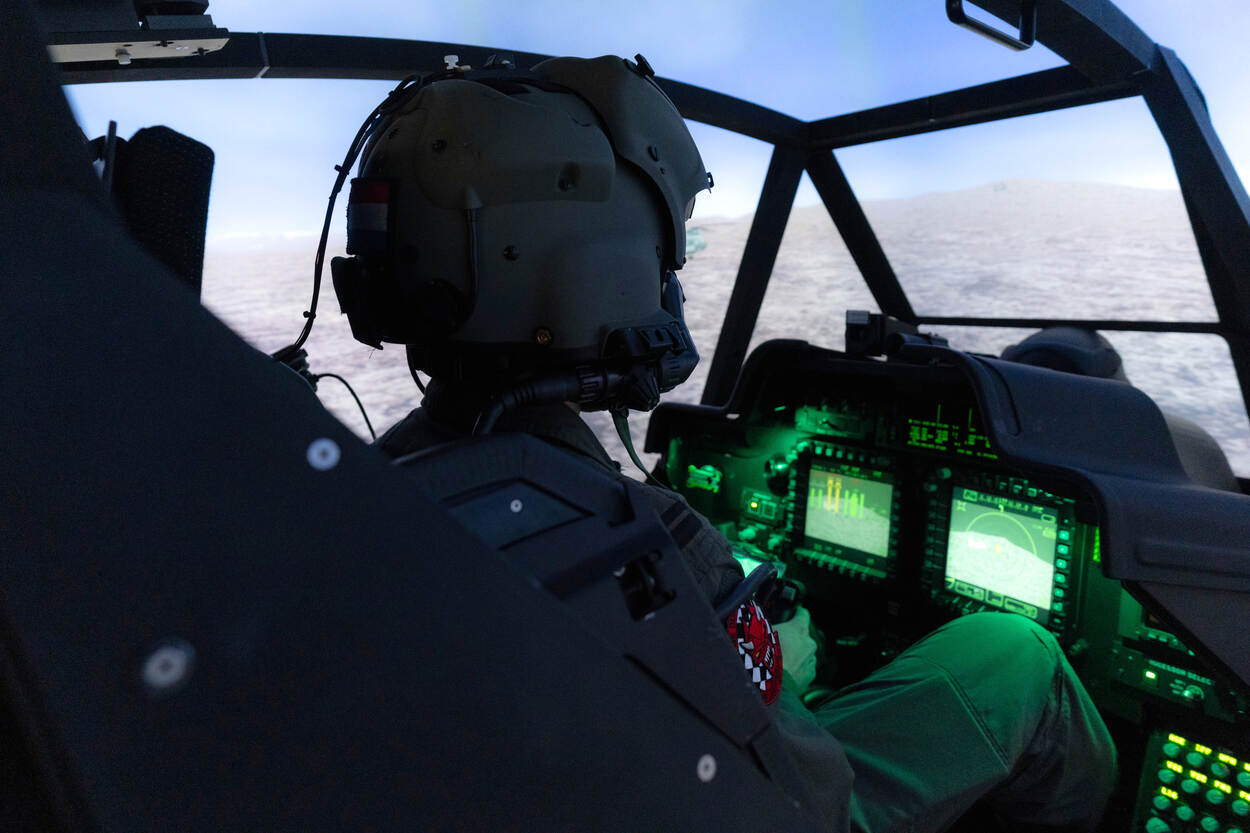 Een vlieger in een simulator van de Apache. Voor hem lichten groene schermpjes op. Het uitzicht bestaat uit een virtuele wereld.