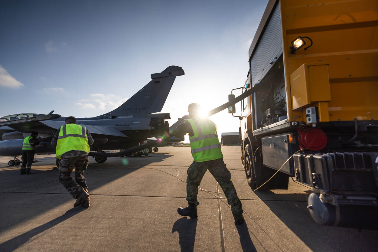 Twee mannen rollen een tankslag uit en lopen daarmee naar een Franse Rafale.