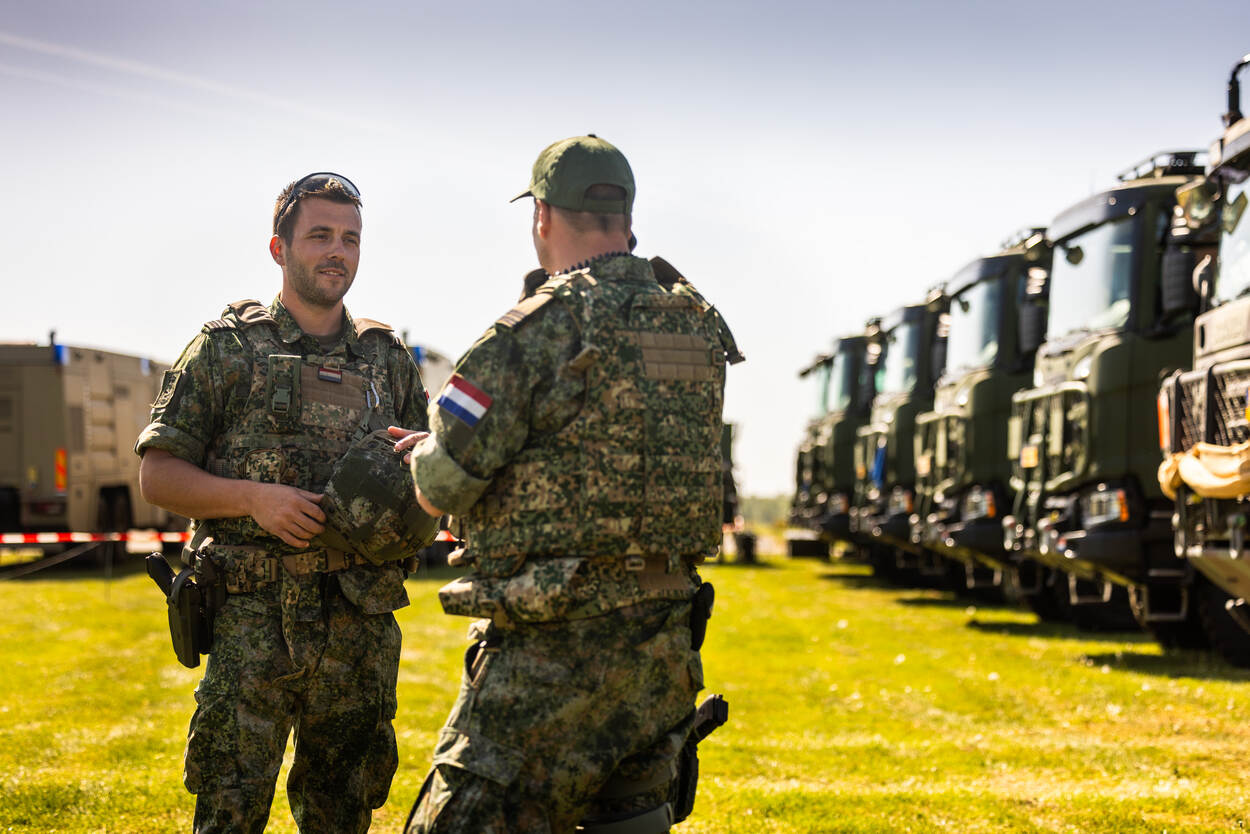 Twee militairen in gesprek naast een rij geparkeerde militaire voertuigen.