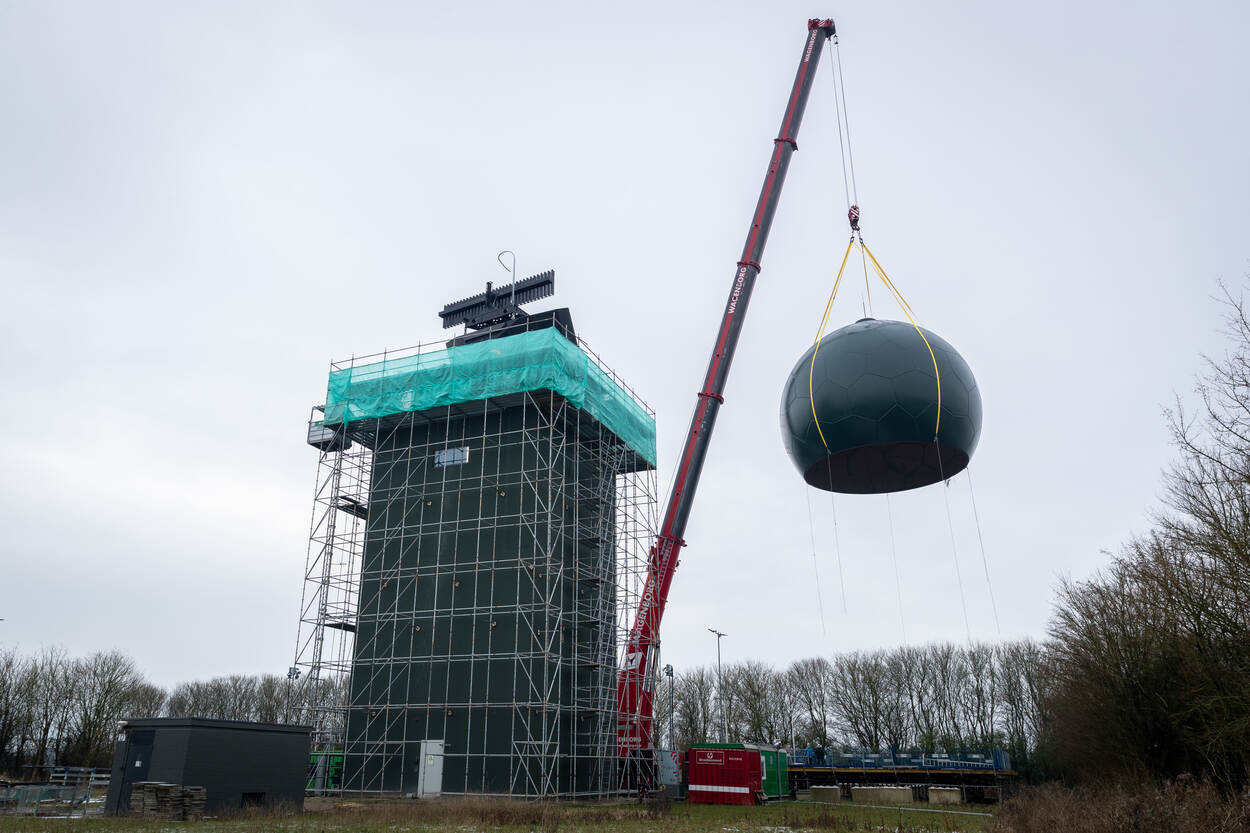 Een hijskraan tilt een bol over een SMART-L-radar die op een toren staat.