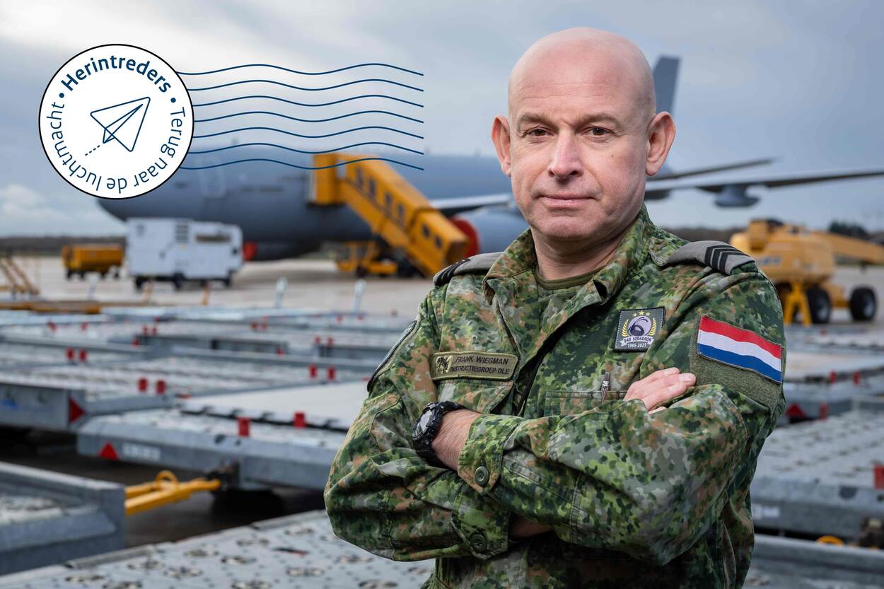 Frank Wiegman in camouflage-uniform op Vliegbasis Eindhoven, staand met gekruiste armen op het platform, met op de achtergrond een militair transportvliegtuig en cargomaterieel.