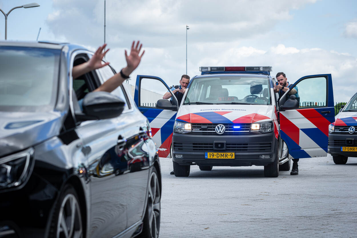 Een man steekt zijn handen uit het raam van een auto. Marechaussees voeren de voertuigprocedure uit.