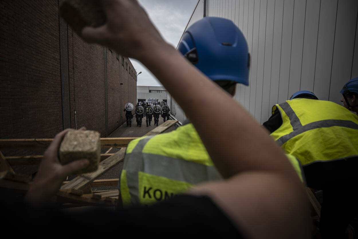 De demonstranten staan achter de barricade. De ME komt op ze af.