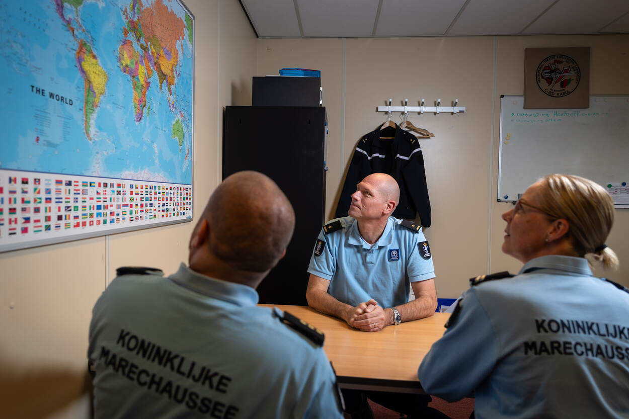 Hoofd BBM en 2 collega's kijken naar een wereldkaart.