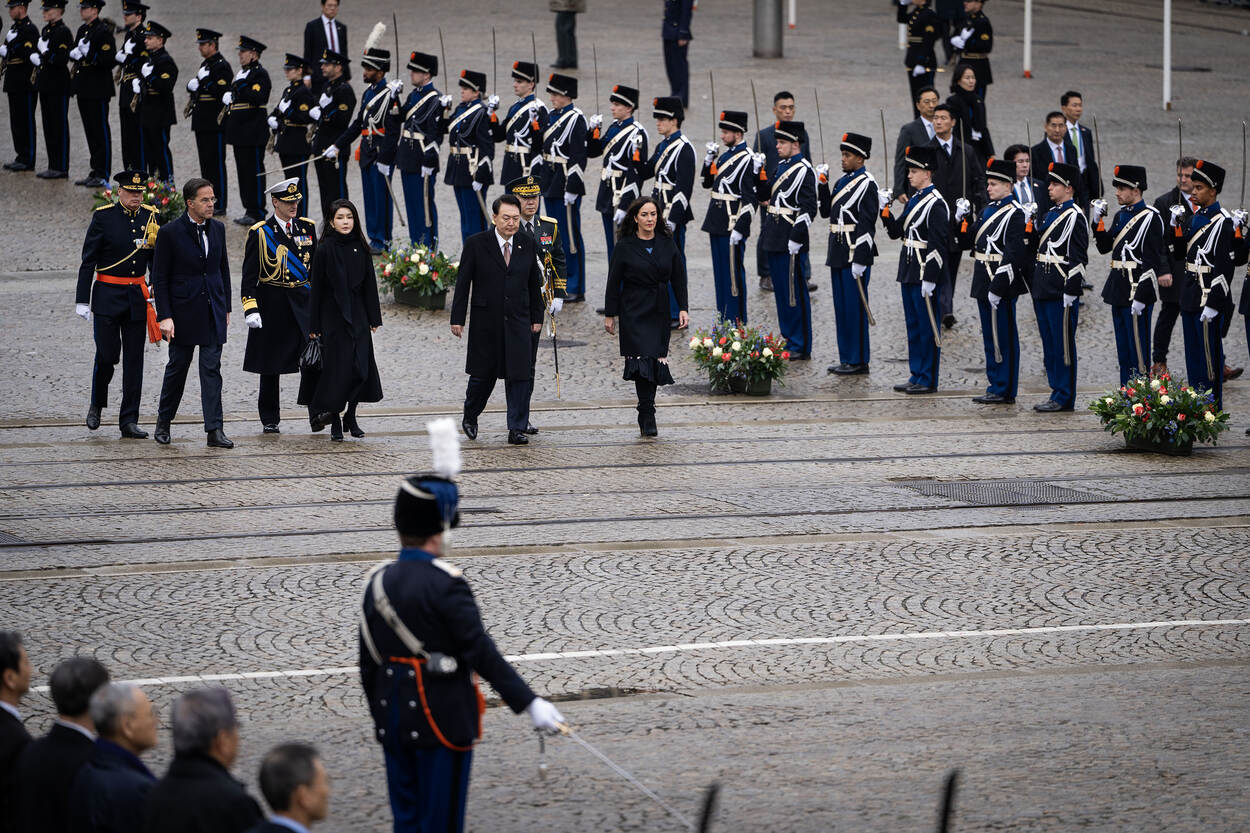 Een overzichtsfoto van het staatsbezoek op de Dam. De Koreaanse president wandelt door een haag van marechaussees.