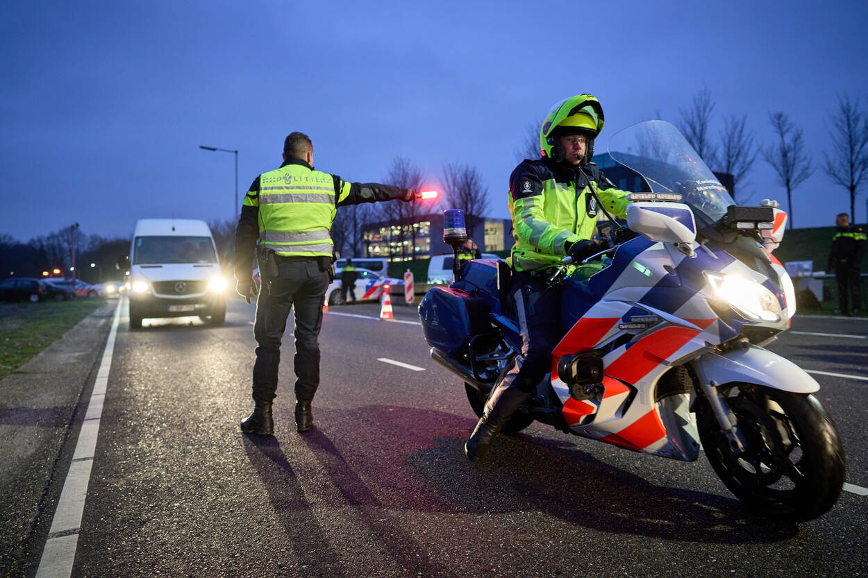 Motorrijder van de Marechaussee begeleidt een wit busje.