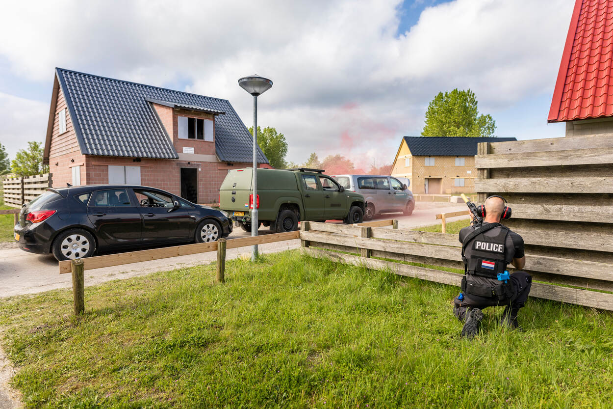 een gewapende persoonsbeveiliger schuilt achter een schutting.