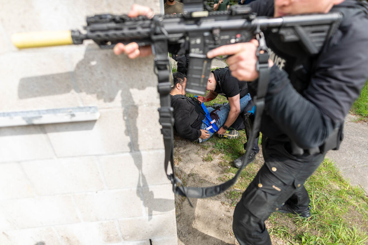Achter een gebouw wordt een gewonden verzorgd terwijl een collega voor dekking zorgt.