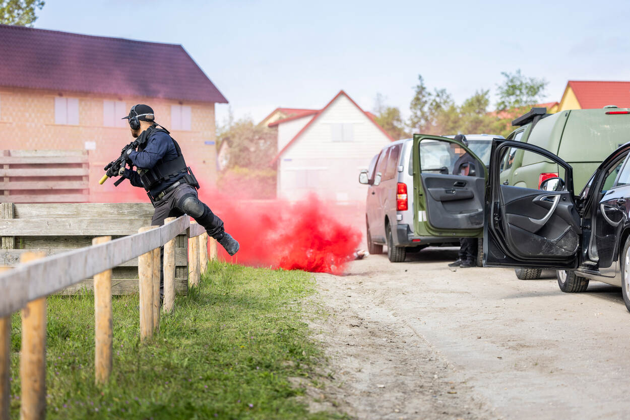Een persoonsbeveiliger stapt over een hek, op de achtergrond is een rode wolk rook te zien.