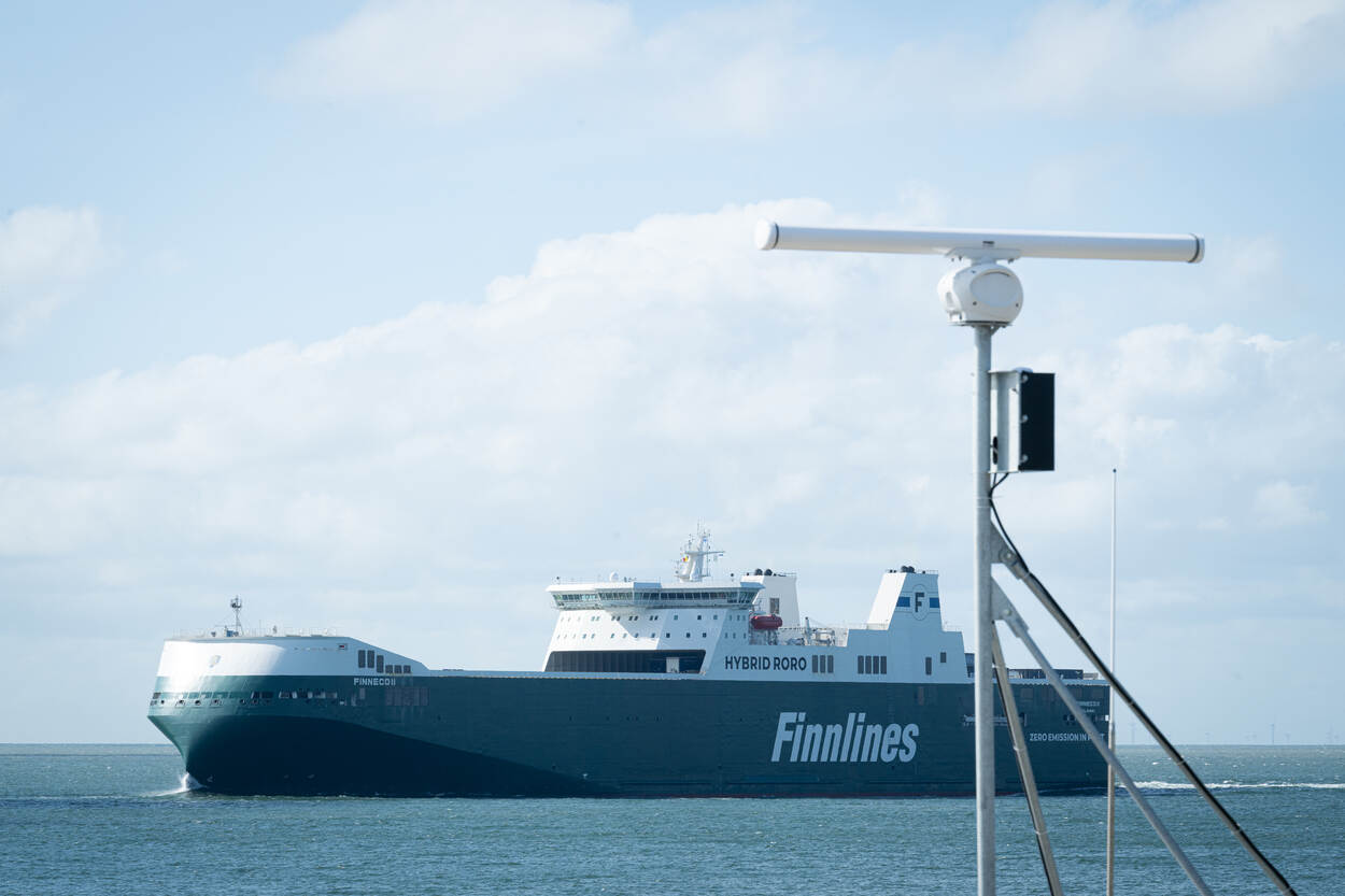 De walradar staat op een paal en monitort de scheepvaart. Op de achtergrond vaart een vrachtschip.