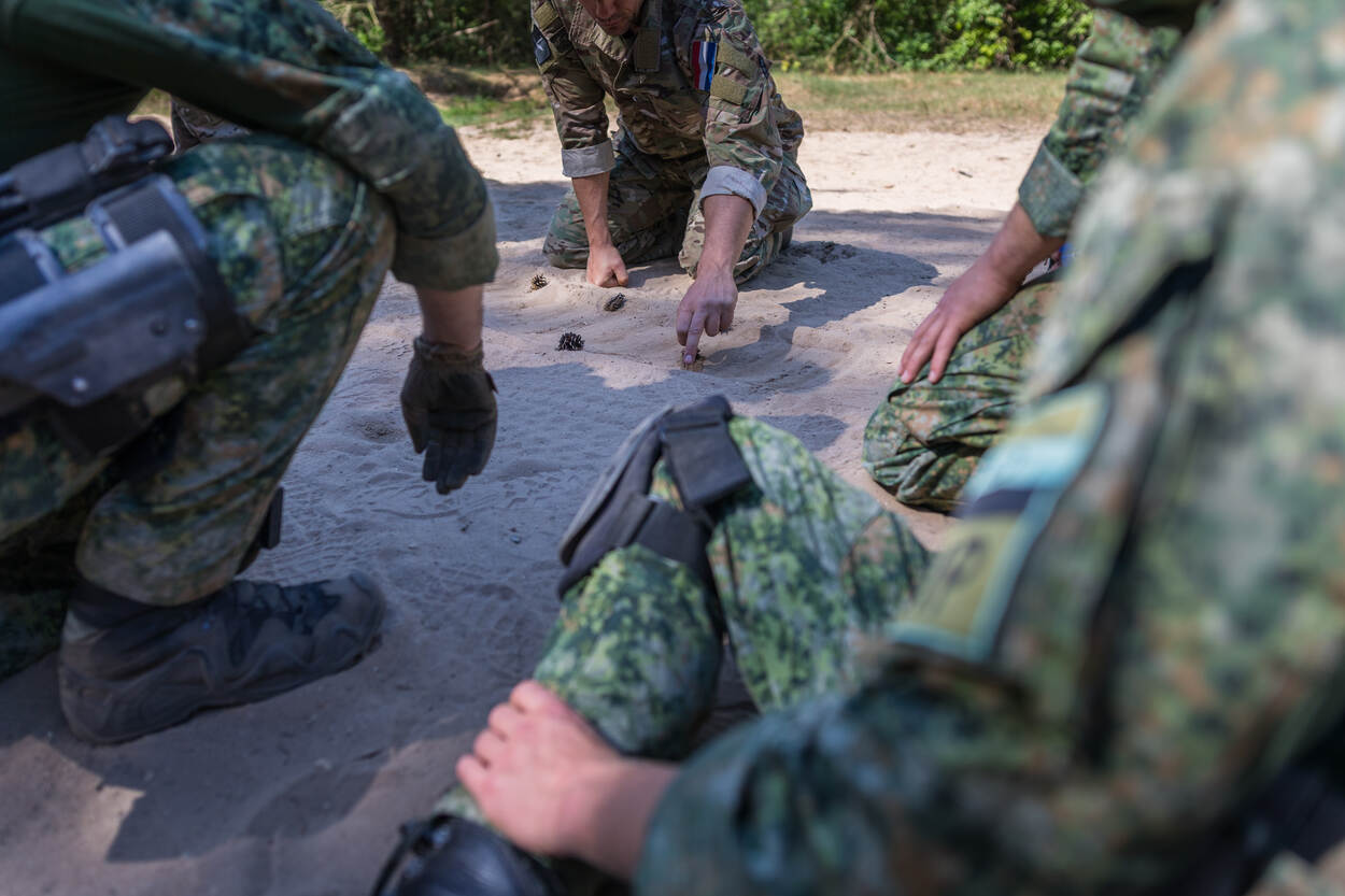 Uitleg door instructeur in het bos, militair van MP op voorgrond.