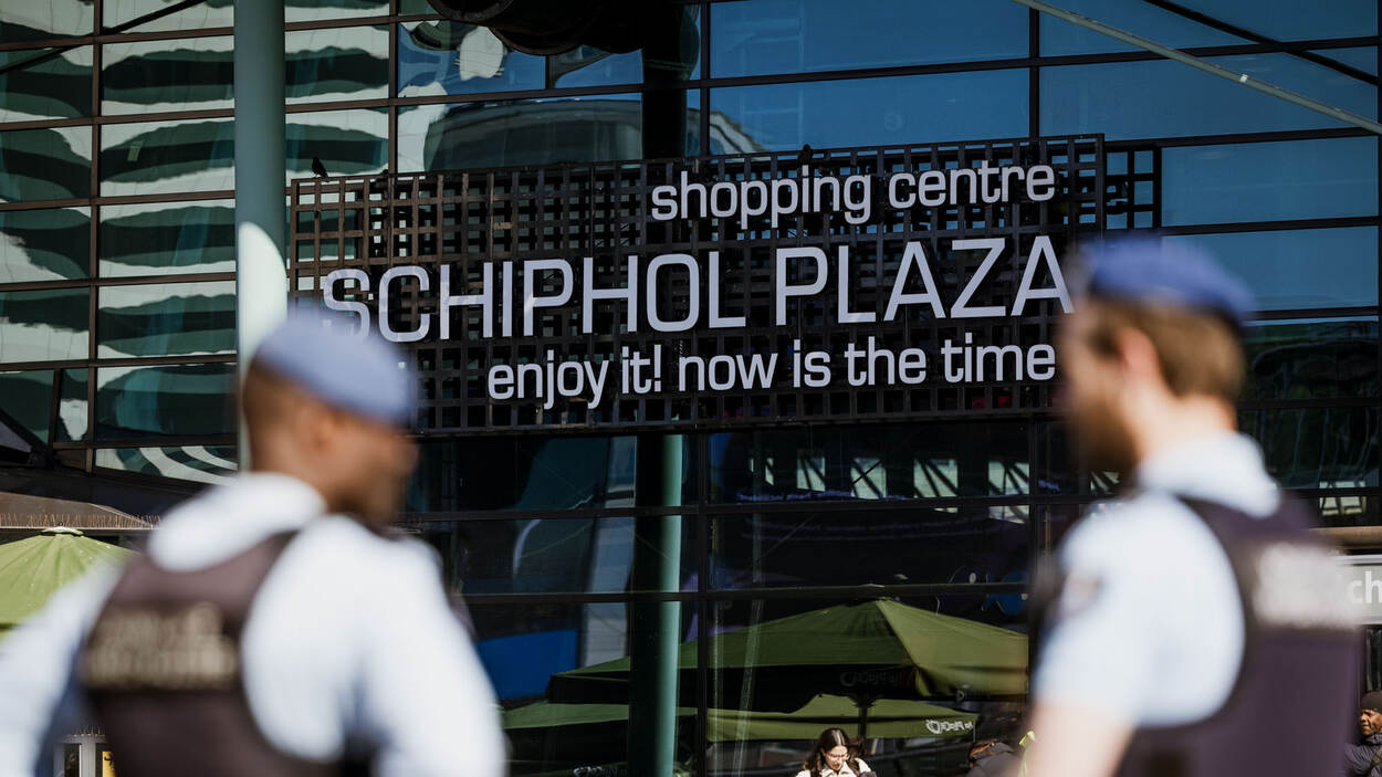 2 leden van de KMar staan voor bord van Schiphol Plaza.