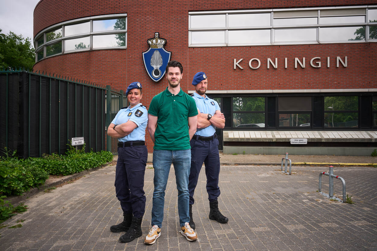 1 burger poseert te midden van 2 leden KMar voor gebouw van de Marechaussee.